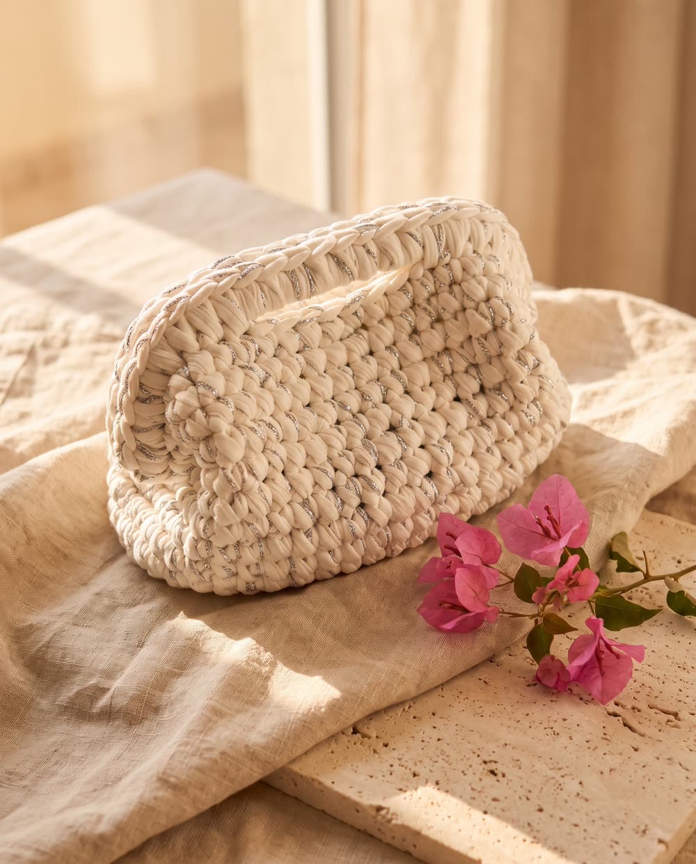 Clutch bianca all'uncinetto su lino e pietra con un rametto di bouganville