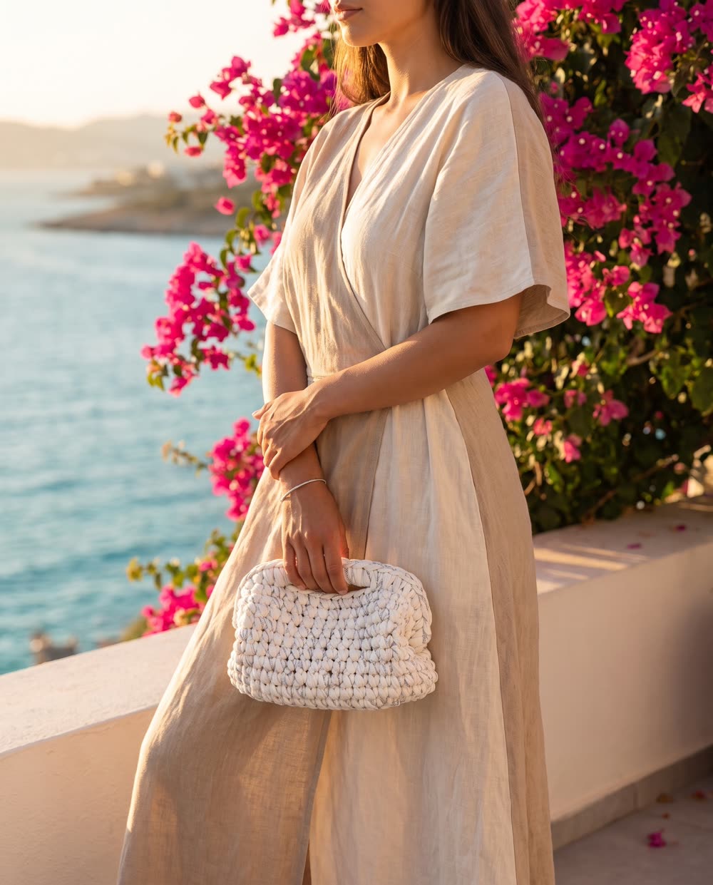 Clutch bianca con filo argento tenuta in mano su una terrazza sul mare al tramonto